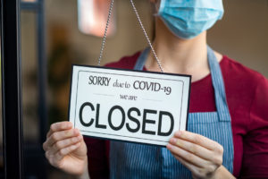 Employee with a medical mask putting a closed sign in a window